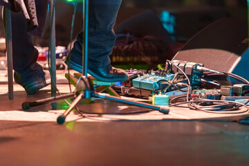 Closeup of a man’s feet pressing knobs on electric guitar pedals during a live performance, controlling sound effects and tone adjustments on stage