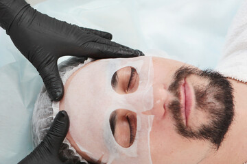 Cosmetologist puts a mask on the man's upper face. A man with a beard. Men's cosmetology. A man in a cosmetology clinic. The concept of youth preservation and skin care.