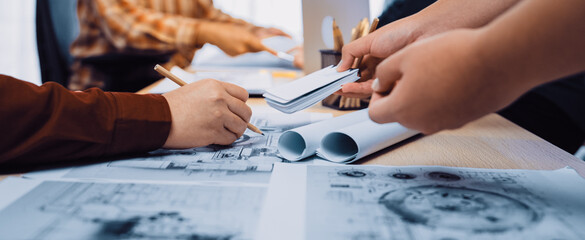 A diverse team collaborates on project planning in a well-lit office, surrounded by architectural drawings and modern technology, enhancing creative brainstorming. SACTR