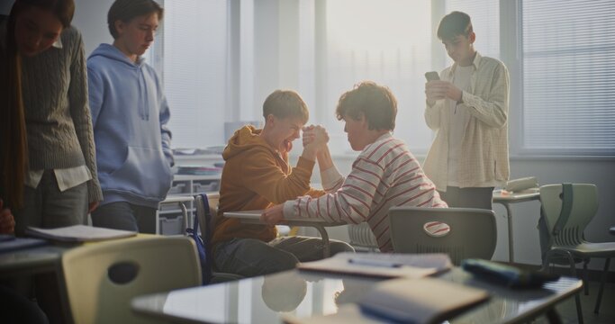 Students Playfully Arm Wrestle at Desk During Break, Surrounded by Laughing Friends. Concept of Youthful Energy, Friendly Competition, and Positive Peer Interaction in Modern School Environment.