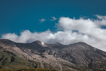 Volcanic steam and clouds over a rocky mountain range of Tokachidake, Daisetsuzan National Park, Biei, Hokkaido, Japan, under a bright, sunny blue sky.