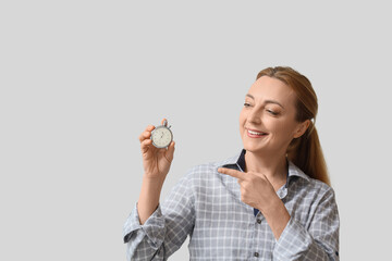 Mature woman pointing at stopwatch on light background