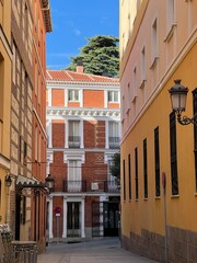 Bright alley with yellow and red facades, wrought iron balconies, and clear blue sky
