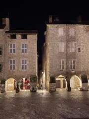 Illuminated medieval square with stone buildings and arched entrances at night