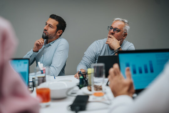 Two colleagues thoughtfully review charts on laptops during a team planning session. - Powered by Adobe