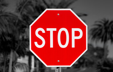 Red and white stop sign on a side road in California. Bright and reflective colors of traffic sign isolated on blurred dark black and white grayscale background. International sign for “STOP”.