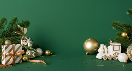 A festive Christmas scene with wrapped gifts, gold baubles and a white train ornament arranged beside pine branches on a green backdrop, conveying seasonal celebration and holiday greeting