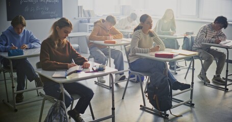 Students Writing Exam In Bright, Modern Classroom. Group of Pupils Sits at Individual Desks Focusing Intently on Taking Exam. Concentration, Independent Study, Academic Workload in Modern Education.