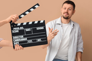 Male actor and female hands with movie clapper on beige background