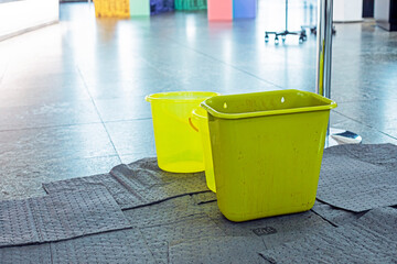 Light green buckets with napkins stand above a leaky ceiling in a public place.