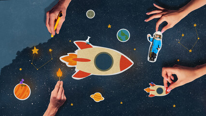 Hands putting together cosmic scene with rocket and astronaut in colorful cosmic composition. Concept of creative learning, STEM activities, childhood imagination, and education through art.