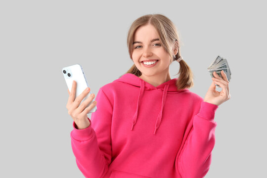 Happy young woman with money and mobile phone on light background. Sports bet concept