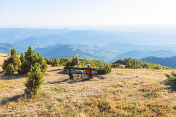 Obraz premium Family enjoying mountain view together from wooden bench at sunset