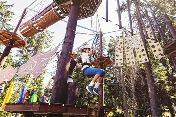Young adventurer crossing elevated rope course in summer forest canopy challenge park