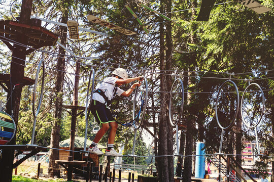Young adventurer crossing elevated rope course in summer forest canopy challenge park
