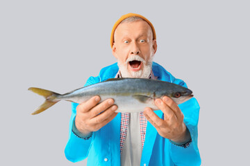 Shocked senior fisherman with fish on light background