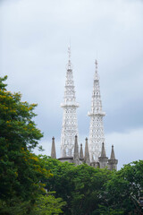 Obraz premium Intricate white Gothic spires of the Jakarta Cathedral, Indonesia, rising above a foreground of lush green trees on a cloudy day