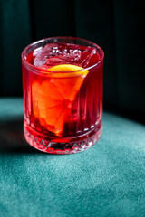 Vibrant red Negroni cocktail with orange slice in a rocks glass, selective focus against a dark background.