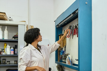 Woman selecting tool from organized workshop pegboard