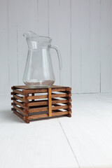 Empty Glass Pitcher on a Wooden Stand Against a White Background