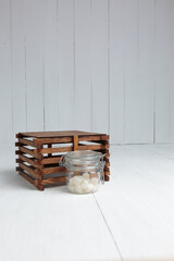 Sugar cubes in a glass jar next to a wooden crate on a white wooden background