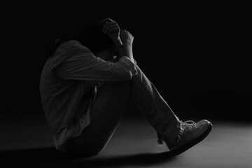 Scared young woman sitting on black background