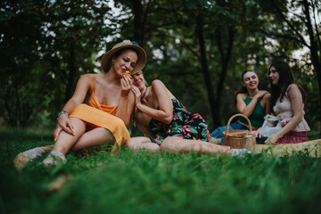 A group of girlfriends picnics on a grassy park lawn. They relax in colorful dresses, share food...