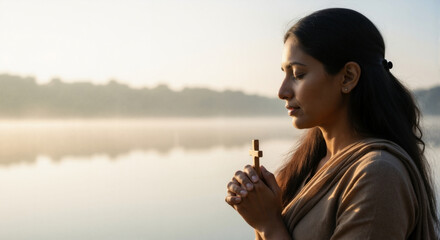 A woman holding a cross in prayer and seeking inner peace in tranquil landscape