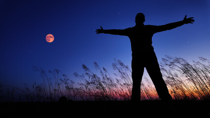 Silhouette of a man and countryside under the Moon, stars and planets in blue hour time.