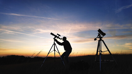 Amateur astro-photographer with a telescope and camera on a tripod photographing night sky with stars, planets, Moon and other celestial objects.