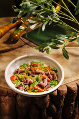A vibrant salad featuring fresh greens, diced meat, and colorful vegetables sits on a rustic wooden table. The warm atmosphere invites enjoyment of this flavorful dish.