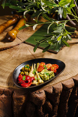 A colorful appetizer platter showcases a variety of fresh ingredients, including olives, roasted tomatoes, and guacamole. Set on a wooden table, it highlights a rustic dining atmosphere.