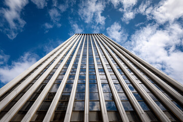 Soaring modern skyscraper photographed from ground level with reflective glass windows, strong vertical lines and dramatic blue sky