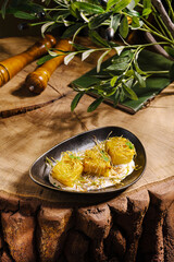 A plate holds three golden pastries made from thin dough, resting on a creamy base. Surrounding the dish are wooden utensils and olive branches, enhancing the rustic feel.