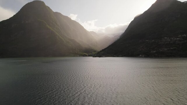 Aerial view of a serene lake surrounded by majestic mountains, their peaks kissed by sunlight, creating a stunning contrast of light and shadow, Odda, Vestland, Norway.