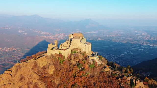 Aerial view of Sacra di San Michele, a beautiful ancient building on top of a mountain surrounded by colorful trees, Piemonte, Italy.