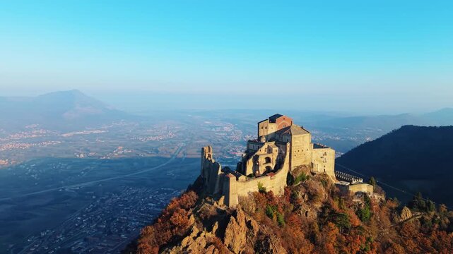Aerial view of the Sacra di San Michele, a stunning abbey perched atop a mountain, with a backdrop of distant mountains, Piemonte, Italy.
