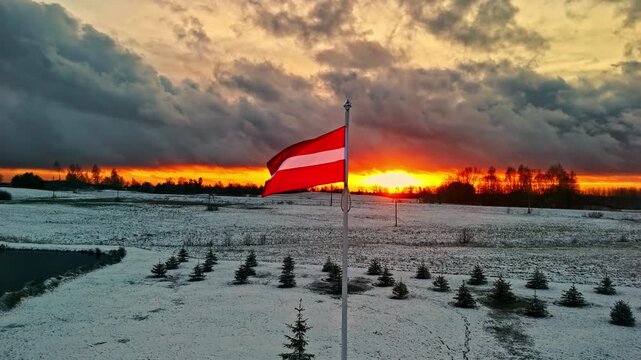 Latvian flag waving in snowy field at sunset, Cesis, Latvia, national pride