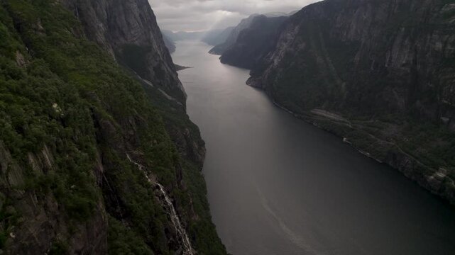 Aerial view of the tranquil, dark waters of Lysefjorden cutting through steep, rocky cliffs under a moody, overcast sky, Lysebotn, Rogaland, Norway.