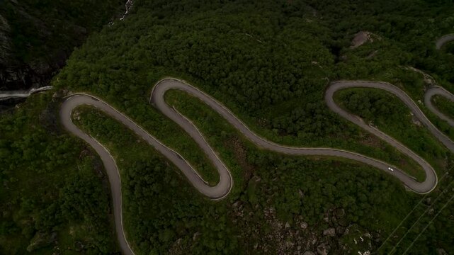 Aerial view of a winding road cutting through lush green mountains with a lone car navigating its curves, Lysebotn, Rogaland, Norway.