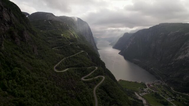 Aerial view of the serpentine road clinging to the steep, verdant mountainsides alongside the serene, reflective waters of Lysefjorden, Lysebotn, Rogaland, Norway.
