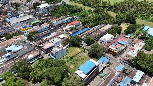 Aerial view of Tenkasi town, highlighting its dense layout of houses and buildings interspersed with greenery. In the distance, lush fields and water bodies are visible.