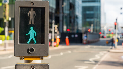 Pedestrian crossing light with green walking figure illuminated on city street in sunlight