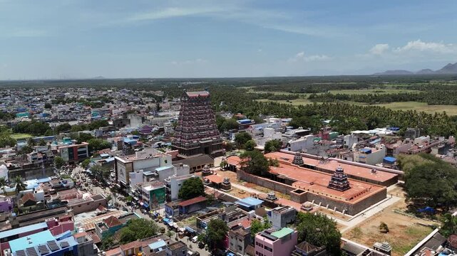 Drone footage of the historic Kasi Viswanathar Temple in Tenkasi, Tamil Nadu, featuring the temple complex, vibrant houses, and scenic green countryside under clear skies.