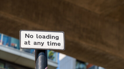 Obraz premium White no loading at any time sign mounted on black pole under city overpass