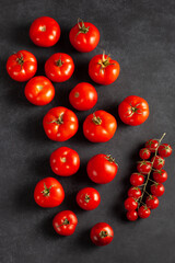 Top view of fresh red tomatoes and cherry tomatoes on dark stone background. Organic ripe vegetables perfect for cooking, healthy eating, vegan recipes, and natural food concepts.
