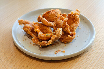 Crispy fried chicken skin served on a gray ceramic plate over a wooden table under natural light. Perfect for restaurant menus, snack product ads, or food blog illustrations