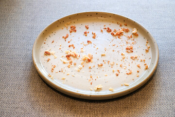 Top view of an empty gray ceramic plate with bread crumbs and food remains on a wooden table in natural light. Perfect for lifestyle blogs, restaurant ads, or food background designs