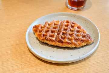 A crispy fish shaped waffle served on a light gray ceramic plate over a wooden table in natural light with a glass of single origin coffee. Perfect for restaurant, homemade bakery, or breakfast menu