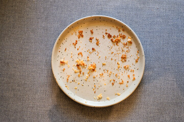 Top view of an empty gray ceramic plate with bread crumbs and food remains on a wooden table in natural light. Perfect for lifestyle blogs, restaurant ads, or food background designs